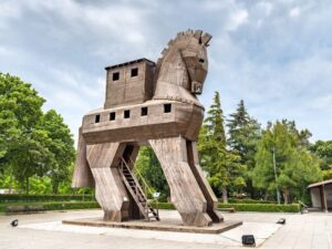 Wooden Trojan Horse sculpture, exterior view, with intricate carvings and large hollow body, set against a clear sky.