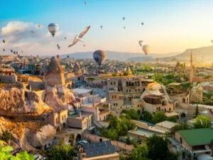 Colorful hot air balloons flying over the fairy chimneys and cave hotels of Goreme, Cappadocia at sunrise.