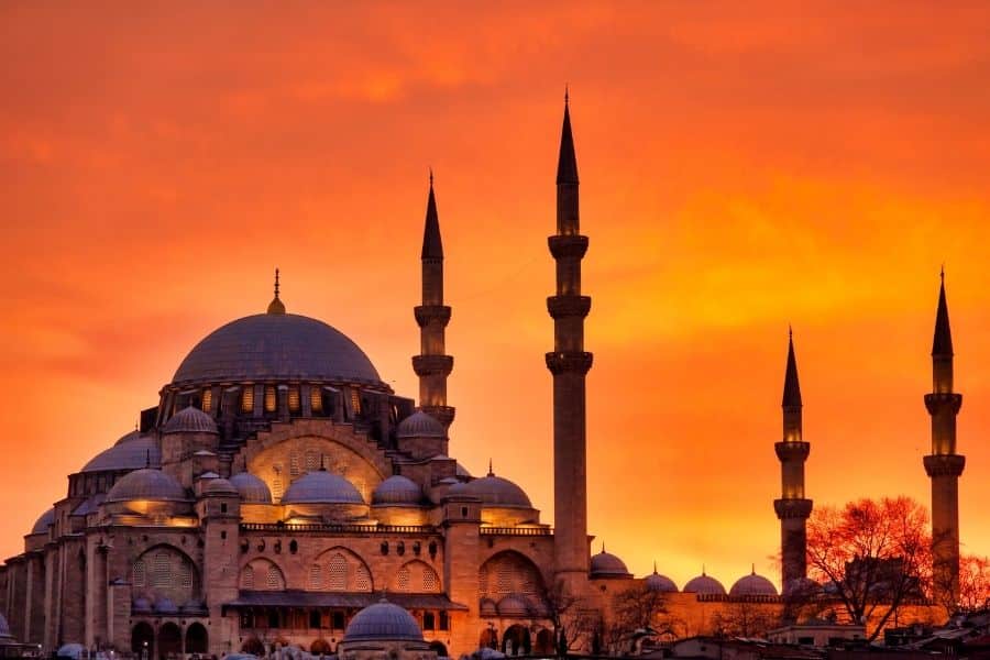 Suleymaniye Mosque in Istanbul silhouetted against a vibrant orange sunset, showcasing its grand domes and towering minarets.