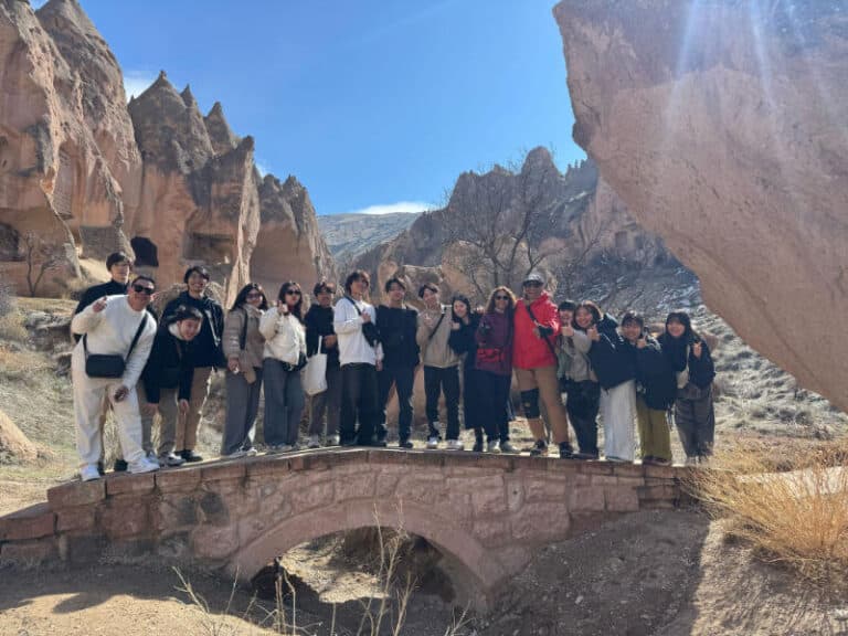 All Istanbul Tours group posing on a stone bridge in Cappadocia, surrounded by iconic rock formations under clear blue skies.