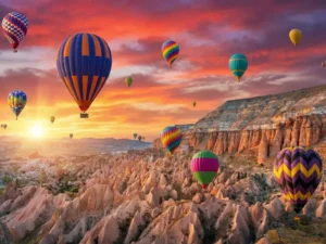 Vibrant multi-colored hot air balloons flying over the rocky landscape and fairy chimneys of Cappadocia, Turkey, during a stunning golden sunrise.