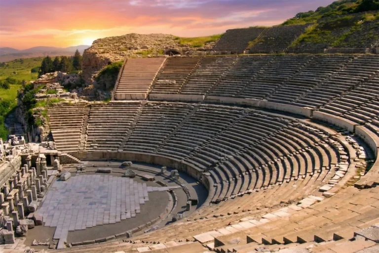 The ancient Great Theatre of Ephesus bathed in beautiful golden sunset light, showing the historic stone seating and stage area without any crowds.